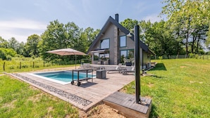 A modern house with a swimming pool, outdoor seating, and a large umbrella.