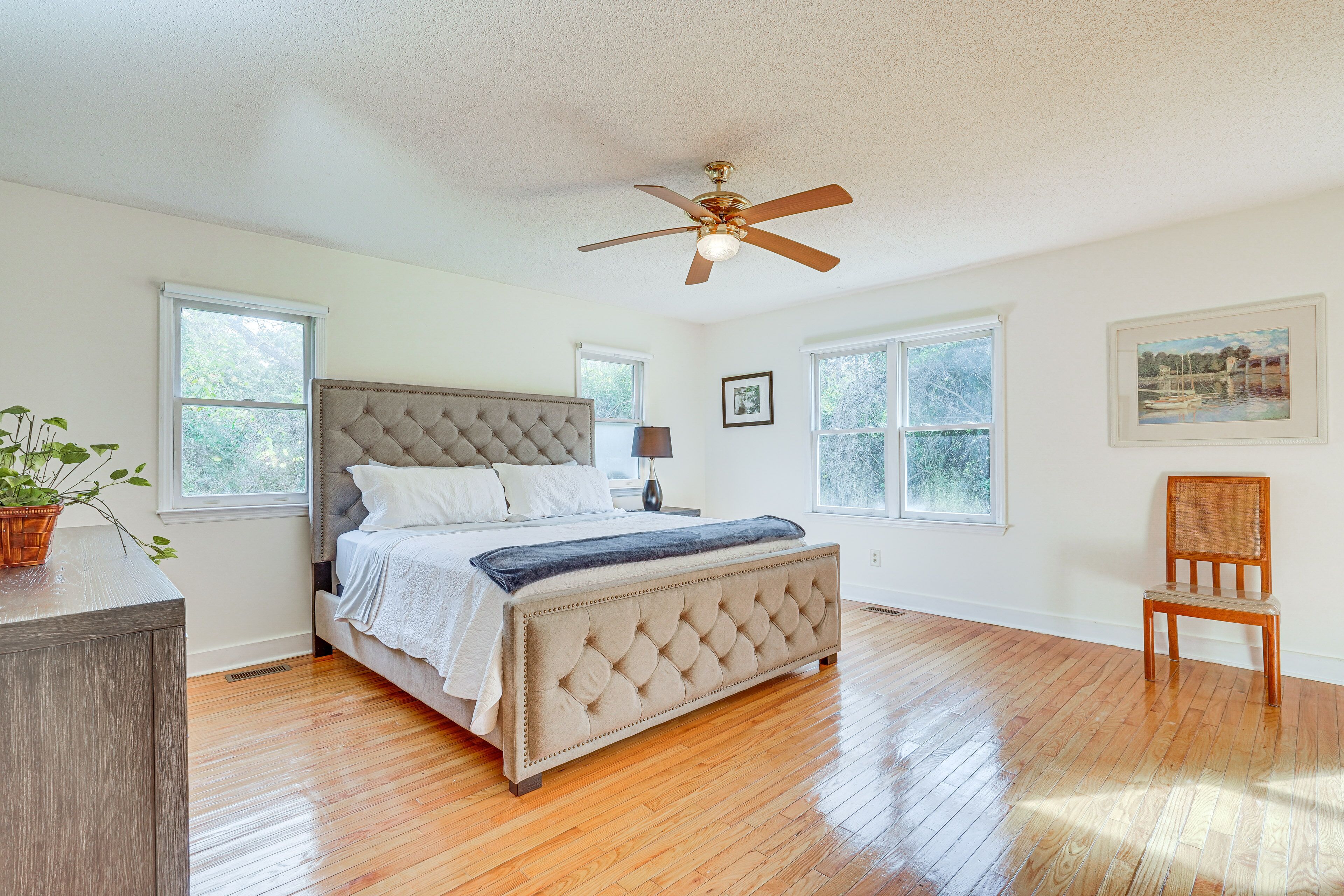 Une chambre à coucher avec un lit, un ventilateur de plafond, une chaise et de grandes fenêtres.