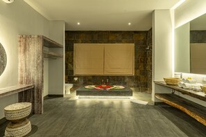 Ein modernes Badezimmer mit Steinwand, einer Holzbank und einem großen Spiegel.