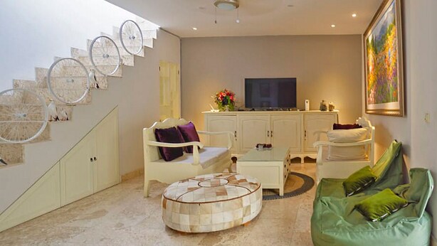 Uma sala de estar com sofá, mesa de centro, televisão e escada com detalhes decorativos.