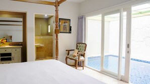 Quarto com cama grande, cadeira de madeira, banheiro e vista para piscina.
