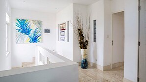 Um corredor com corrimão branco, uma pintura abstrata azul, um vaso com galhos e piso de azulejos.