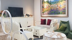 Uma sala de estar com sofá, um banquinho e televisão sobre um móvel.