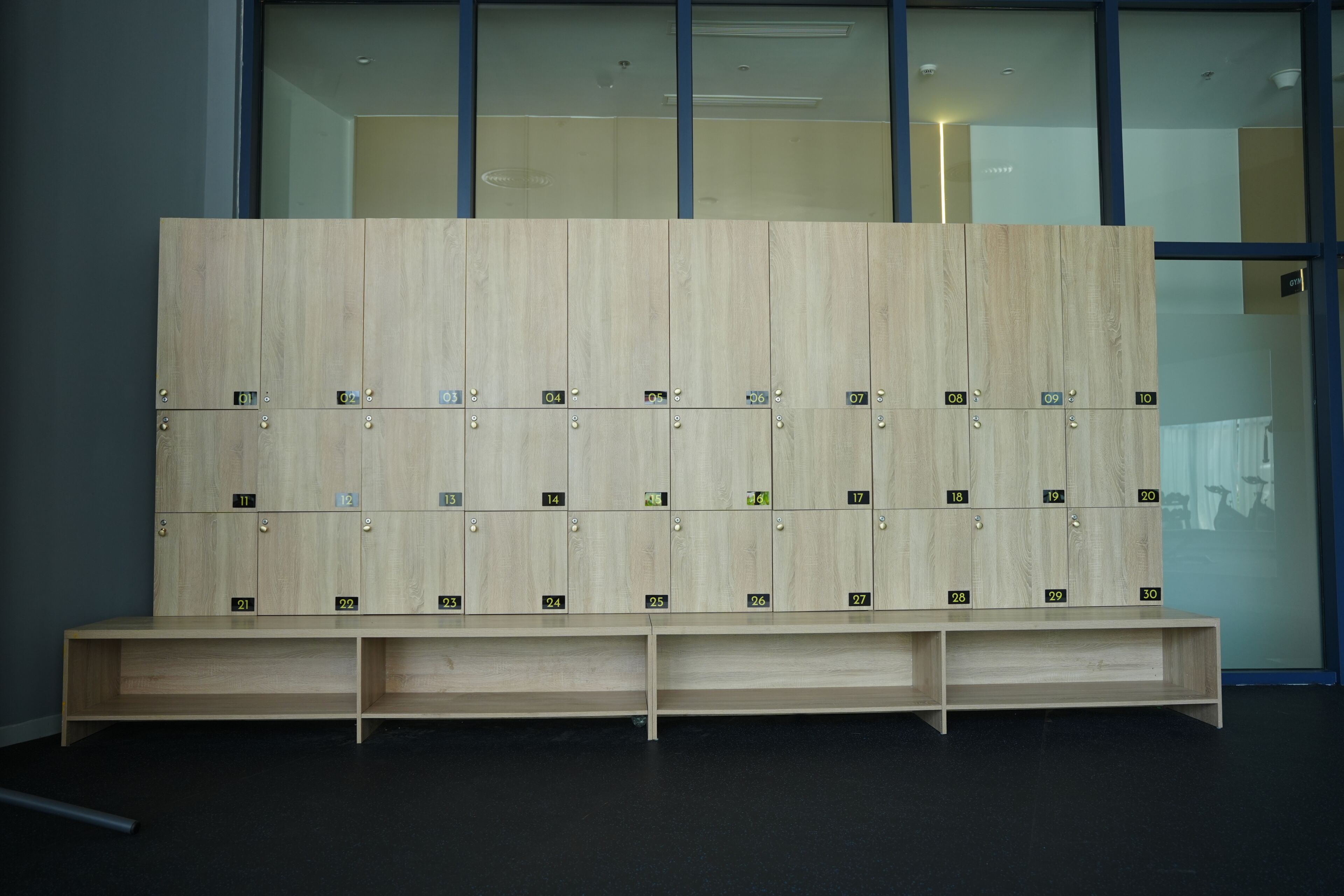 A row of wooden lockers with numbered compartments, a bench in front, and a glass wall in the background.