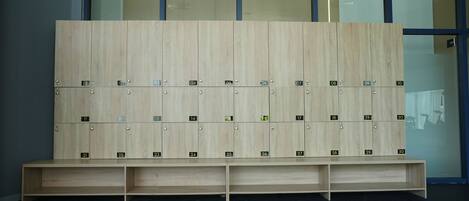 A row of wooden lockers with numbered compartments, a bench in front, and a glass wall in the background.