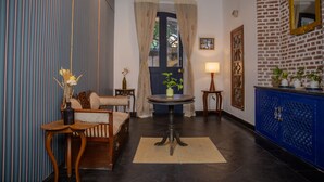 Quarto com sofá, mesa redonda pequena, luminária, armário azul e porta com cortinas.