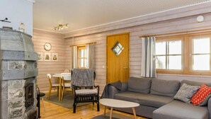 Ein gemütliches Wohnzimmer mit Kamin aus Stein, einem grauen Sofa, einem Couchtisch und einem Essbereich mit Tisch und Stühlen.