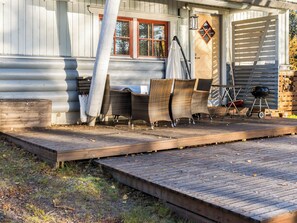 Una terraza de madera con mobiliario exterior, una parrilla y un espacio cubierto con mesa y sillas.