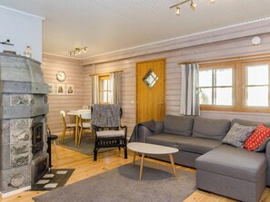 Una sala de estar acogedora con chimenea de piedra, un sofá gris, una pequeña mesa redonda y una mesa de comedor de madera con sillas.