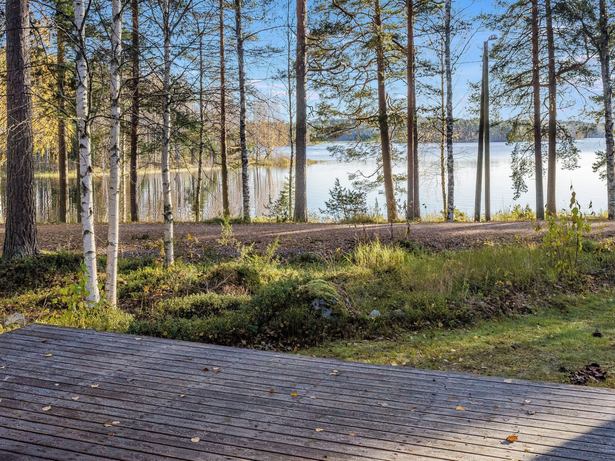 Une terrasse en bois qui mène à une zone boisée, avec un lac en arrière-plan.