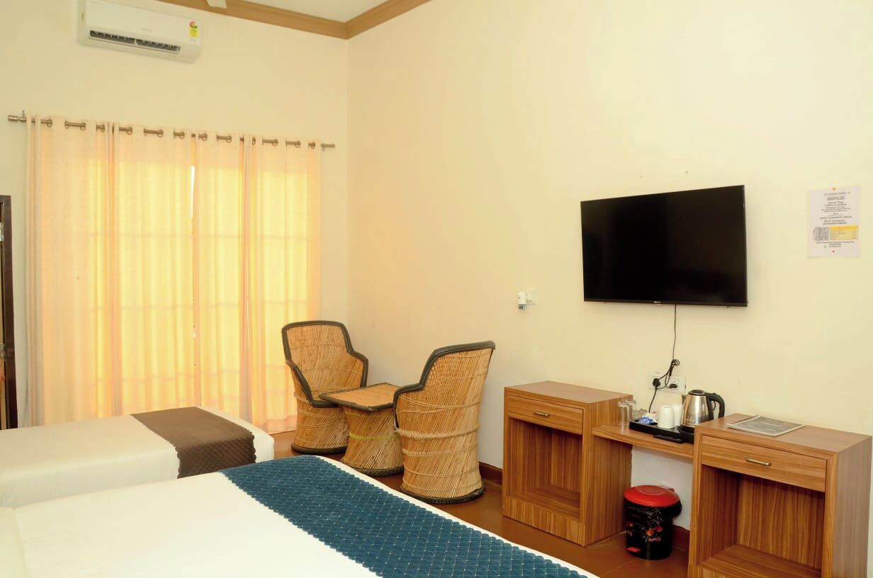 A hotel room with two beds, a desk with a television, wicker chairs, and a small kitchenette.