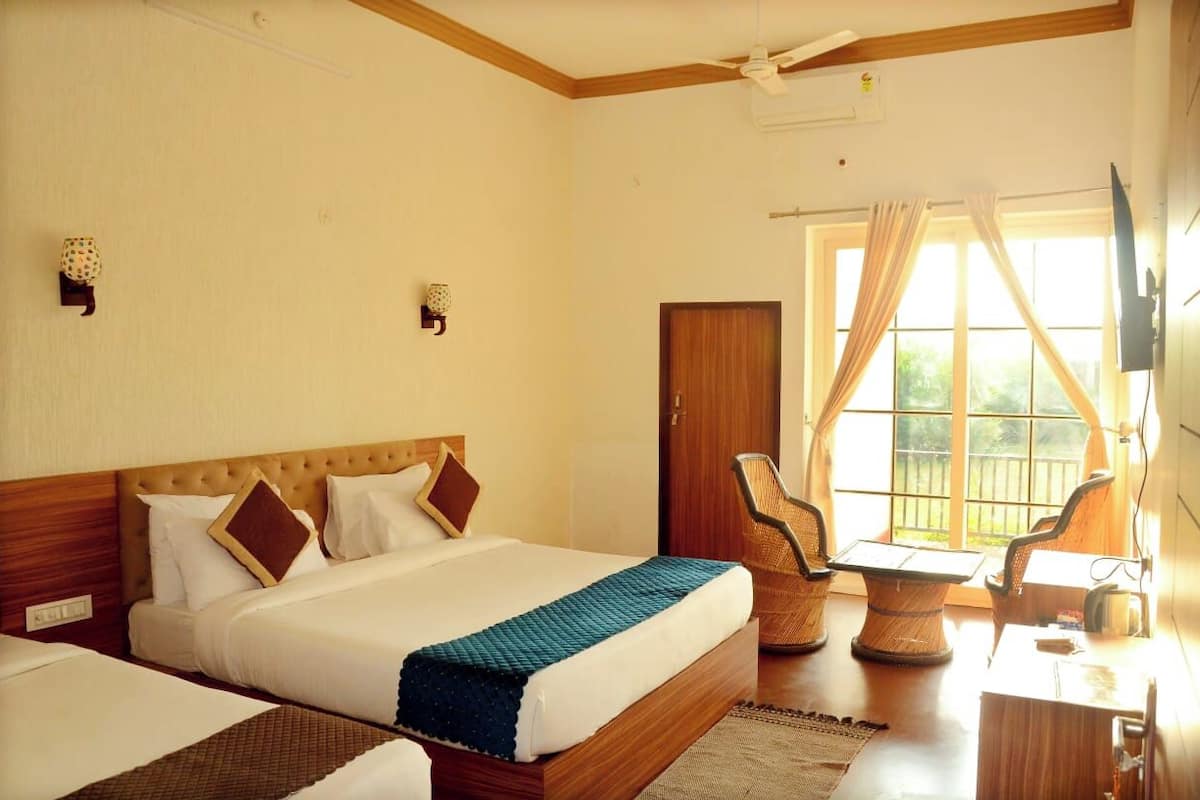 A hotel room with a bed, a desk, and a chair. There is a window with curtains and a view of greenery outside.
