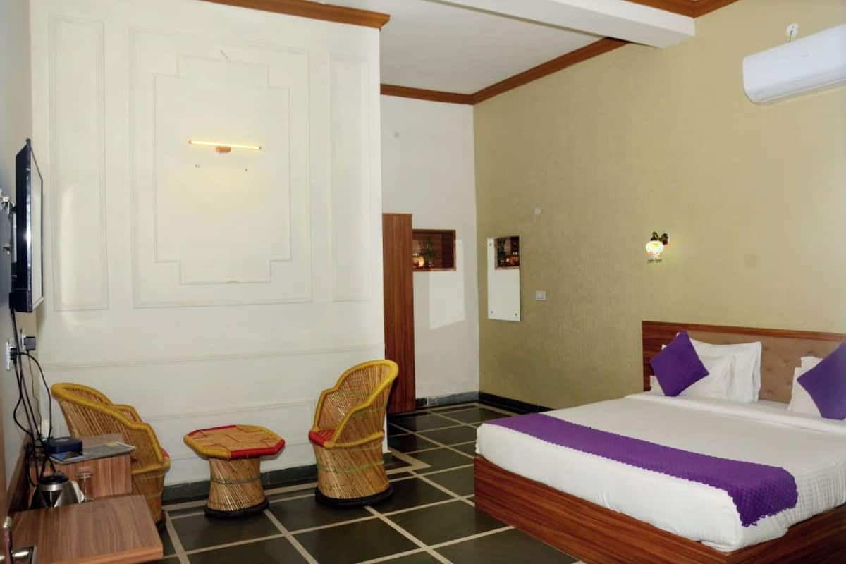 A hotel room with a bed, two wicker chairs, a small table, a television, and a wall-mounted light.