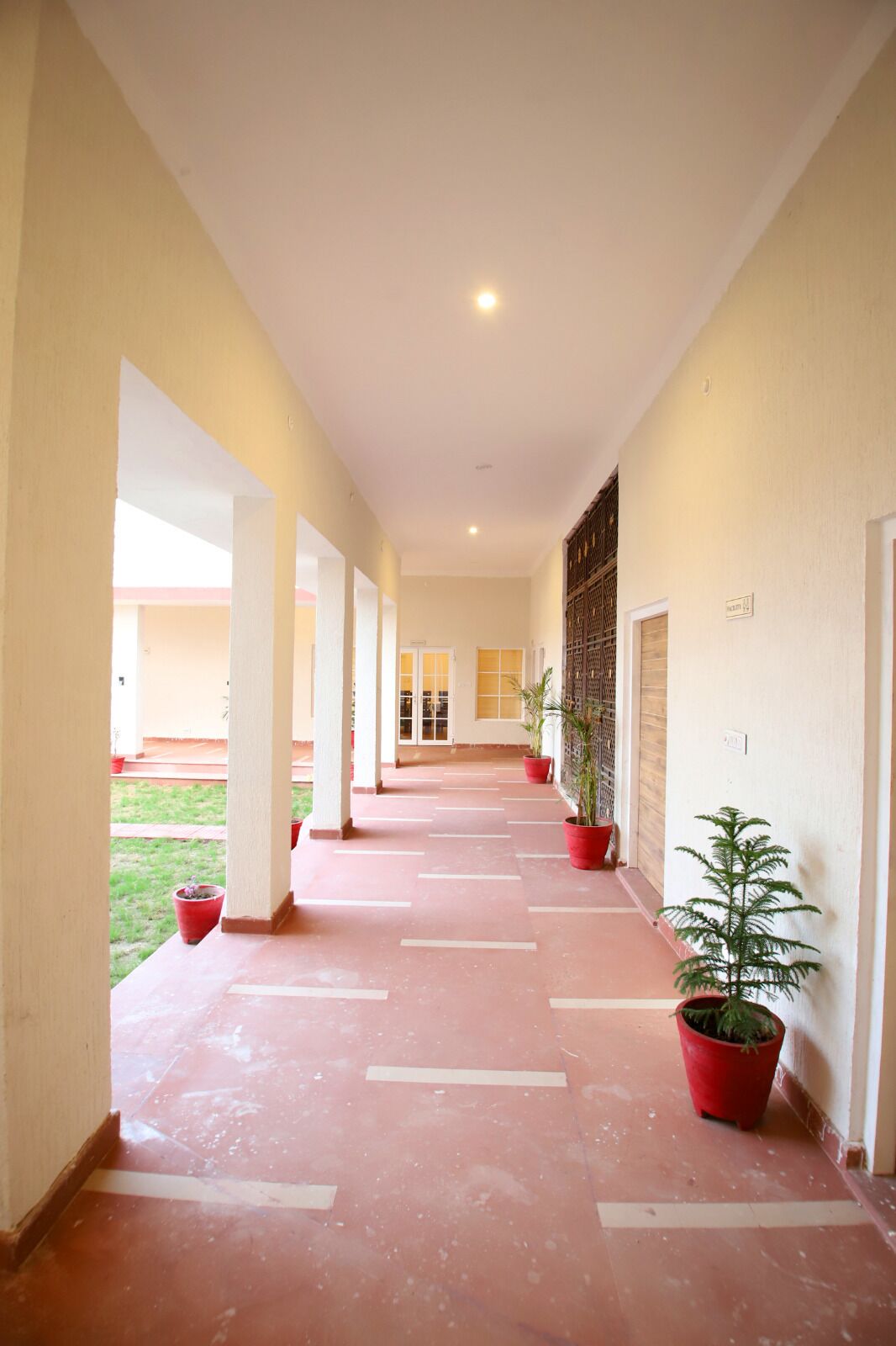 A corridor with red-tiled flooring, white pillars, and potted plants.