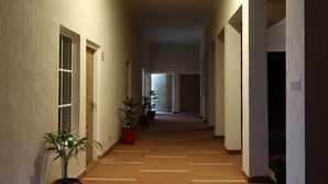 A long, narrow hallway with a tiled floor, potted plants, and doors on both sides. - The Vanashva (Rajgarh)