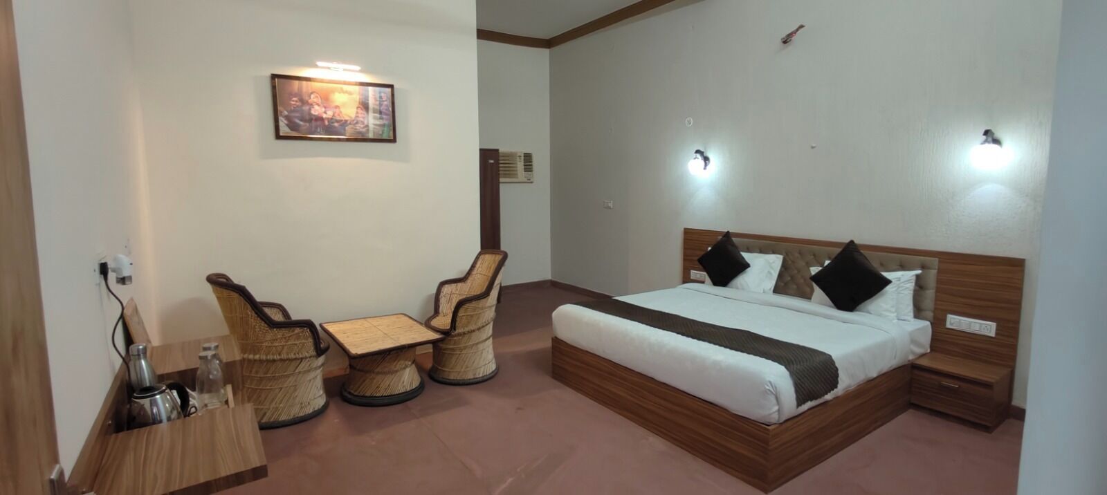 A bedroom with a bed, bedside tables, a chair, a small table, and a wall-mounted light fixture.