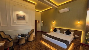 A hotel room with a large bed, a seating area with chairs, a wall-mounted air conditioner, and a view of the outdoors. - The Vanashva (Rajgarh)