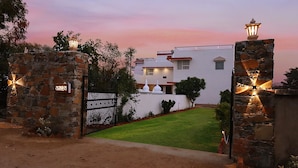 A gated entrance with stone pillars and a white building with a flat roof and a small white structure on the roof. - The Vanashva (Rajgarh)