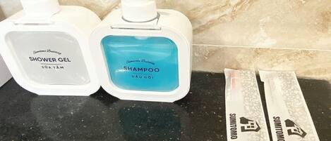 Two bottles of shower gel and shampoo on a black countertop.