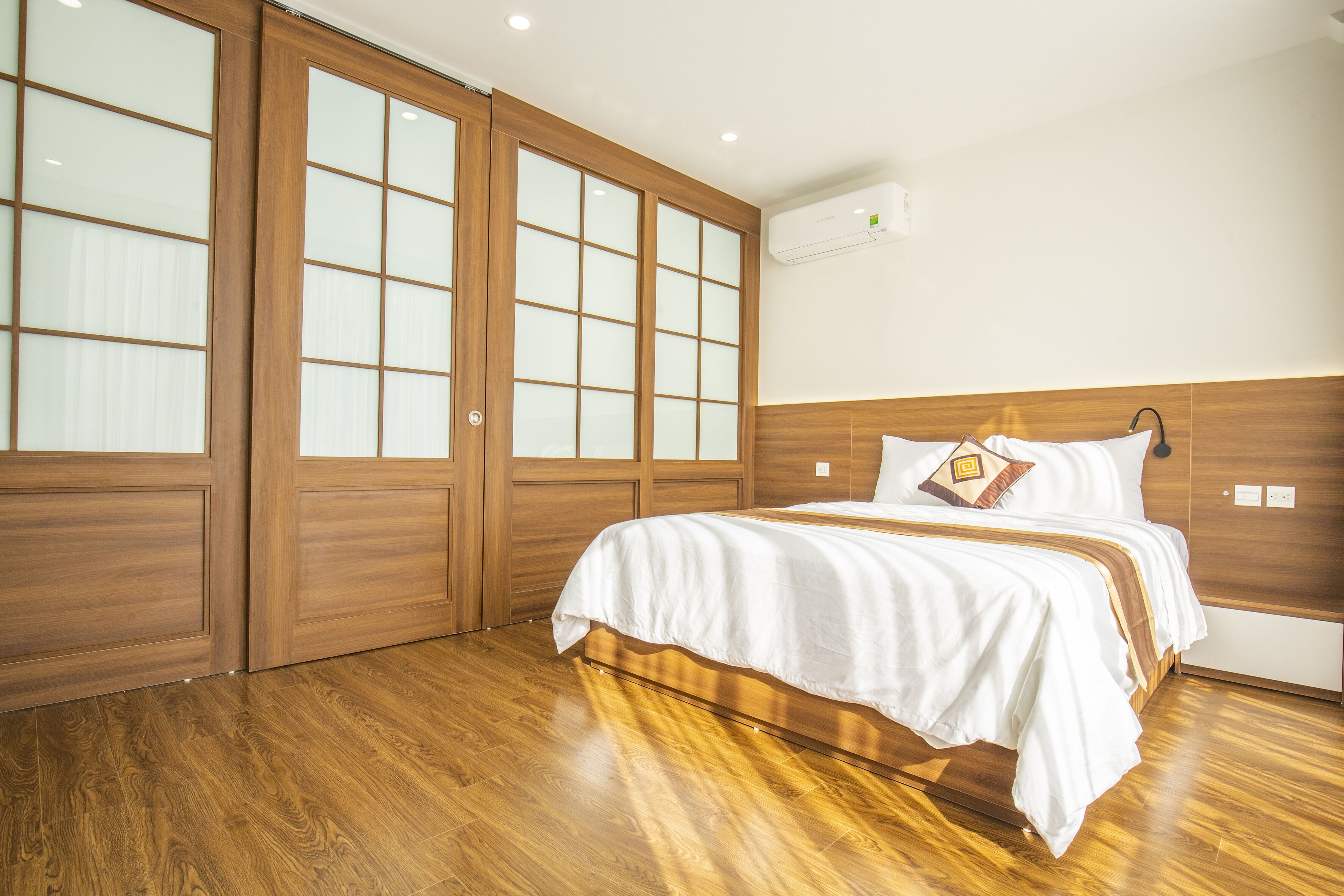 A bedroom with a wooden floor, a bed with white bedding, and a large window with frosted glass panels.