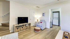 Un salon avec un téléviseur, un canapé, un pouf et un escalier.