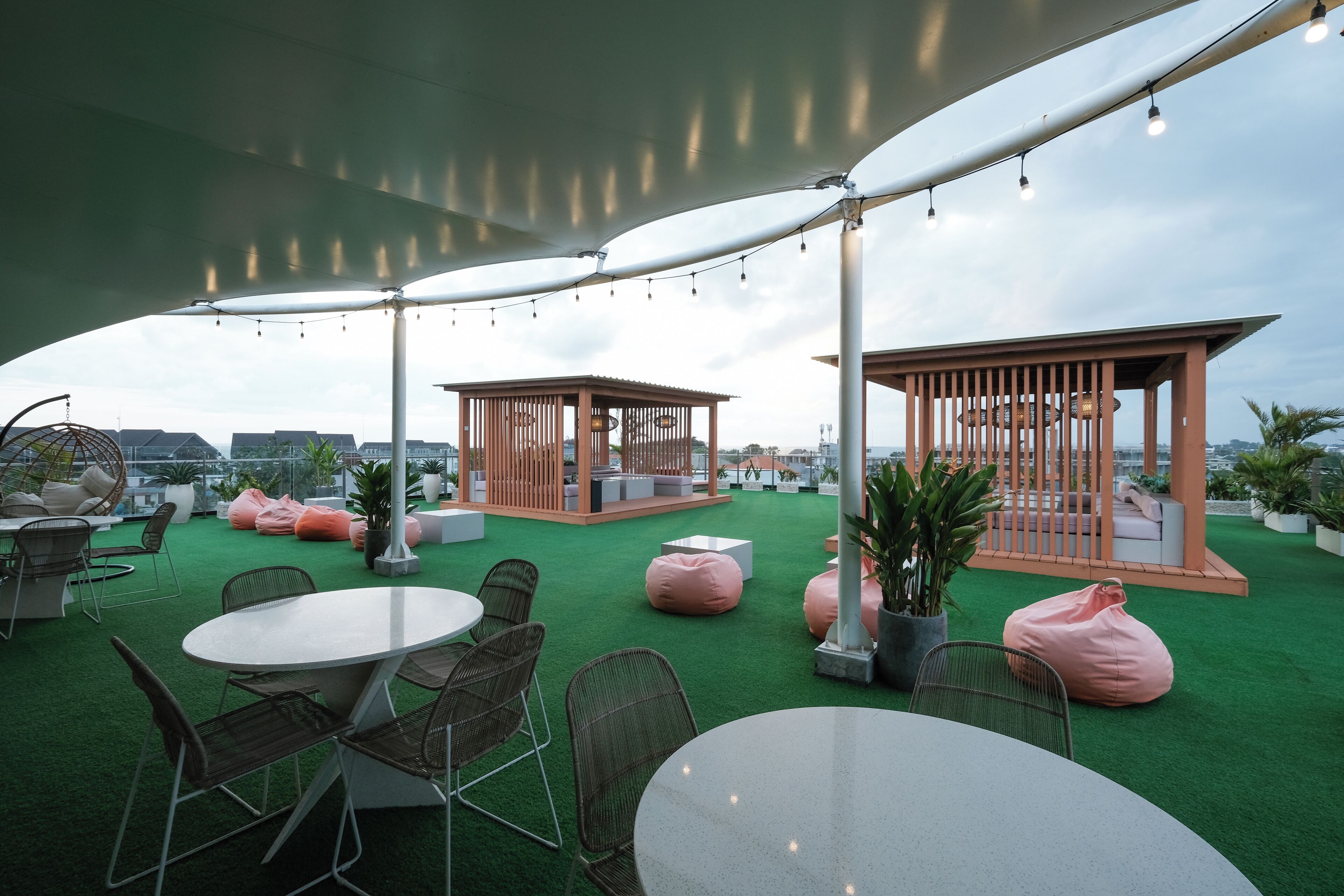 An outdoor seating area with round tables and chairs, a gazebo, and green artificial turf.