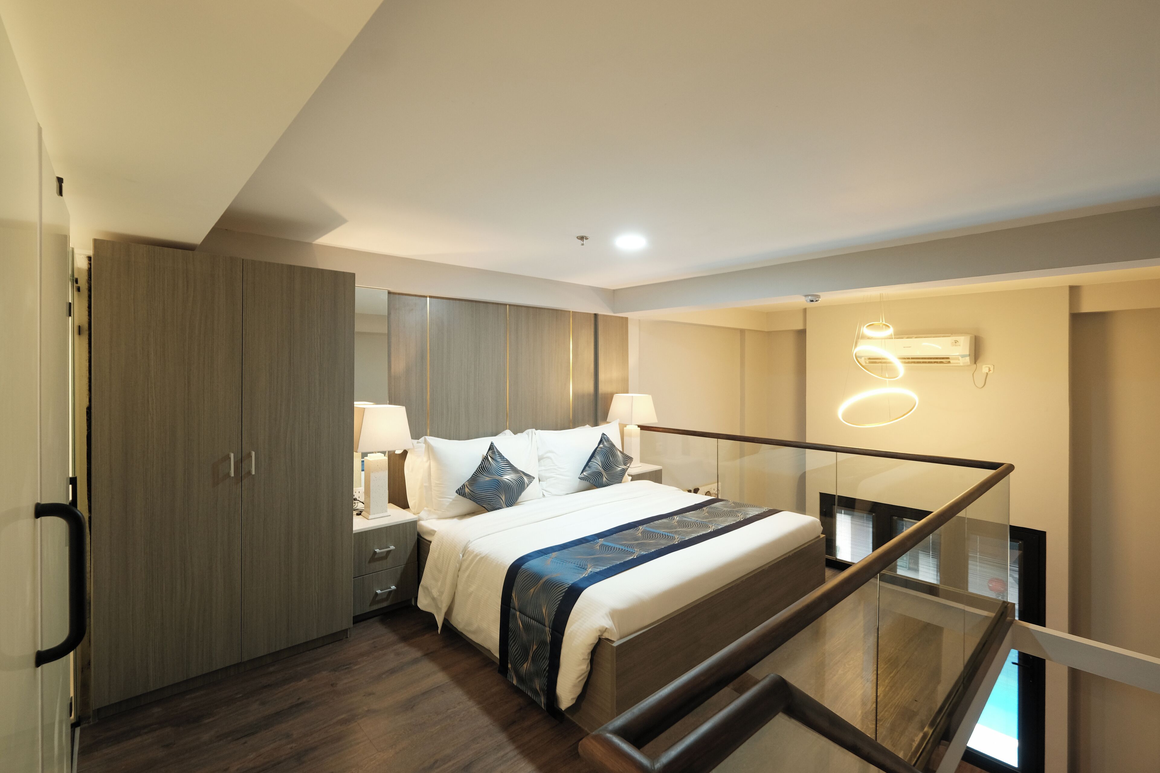 A modern hotel room with a large bed, a glass staircase, and a wooden wardrobe.
