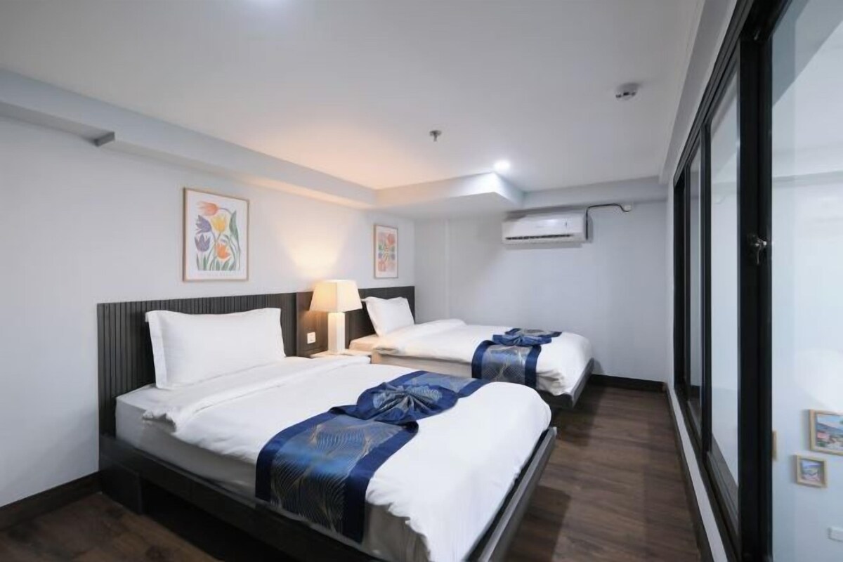 Een hotelkamer met twee bedden, een groot raam en een airconditioner aan de muur.