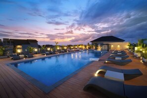A swimming pool with lounge chairs and a covered area, surrounded by buildings and palm trees.