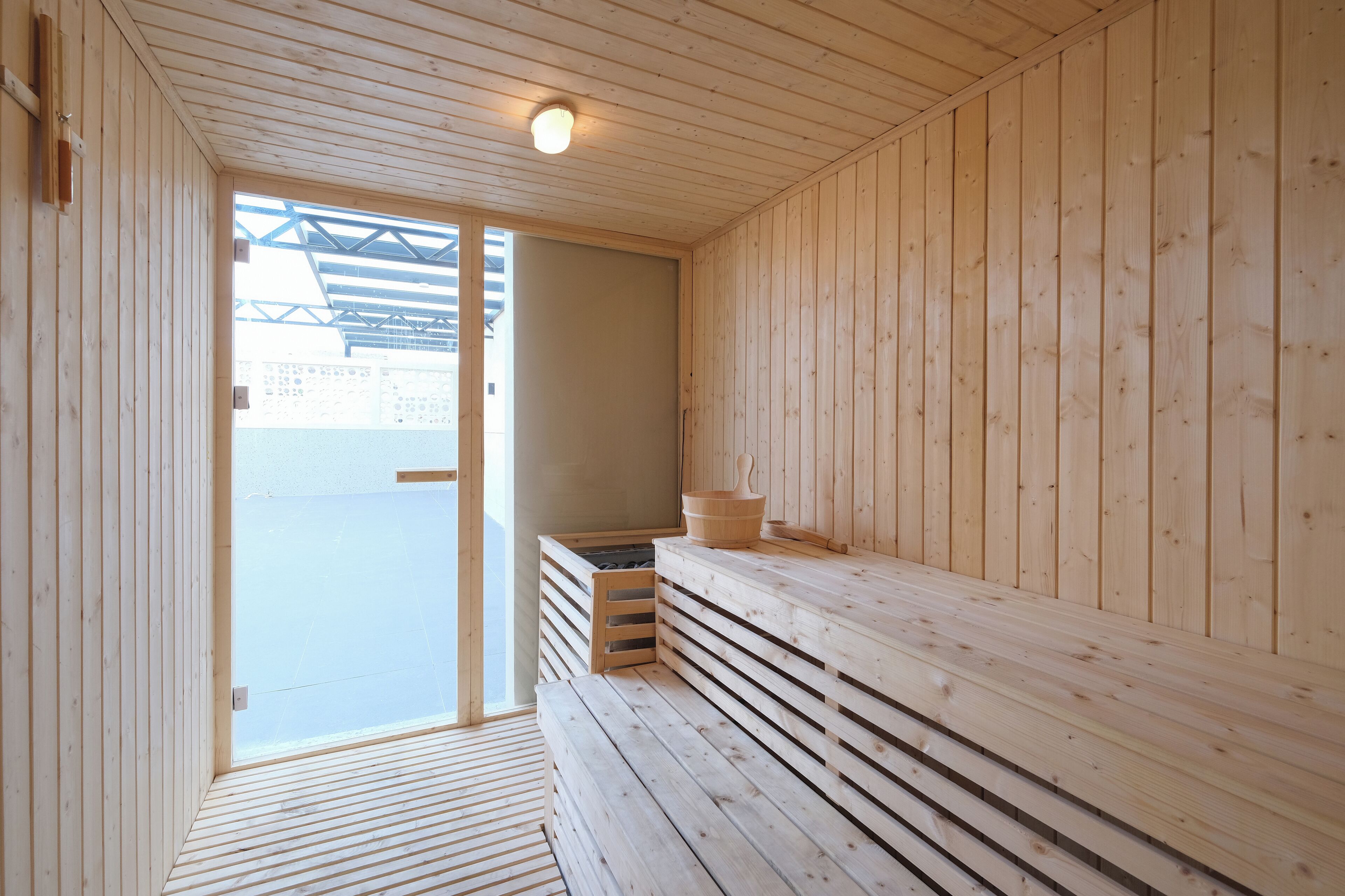 A wooden sauna with benches and a bench seat, a wooden floor, and a ceiling light.