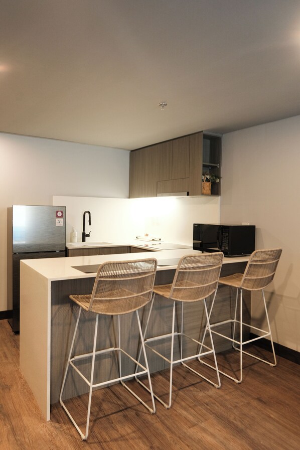 A modern kitchen with a central island, bar stools, a refrigerator, a microwave, and a sink.