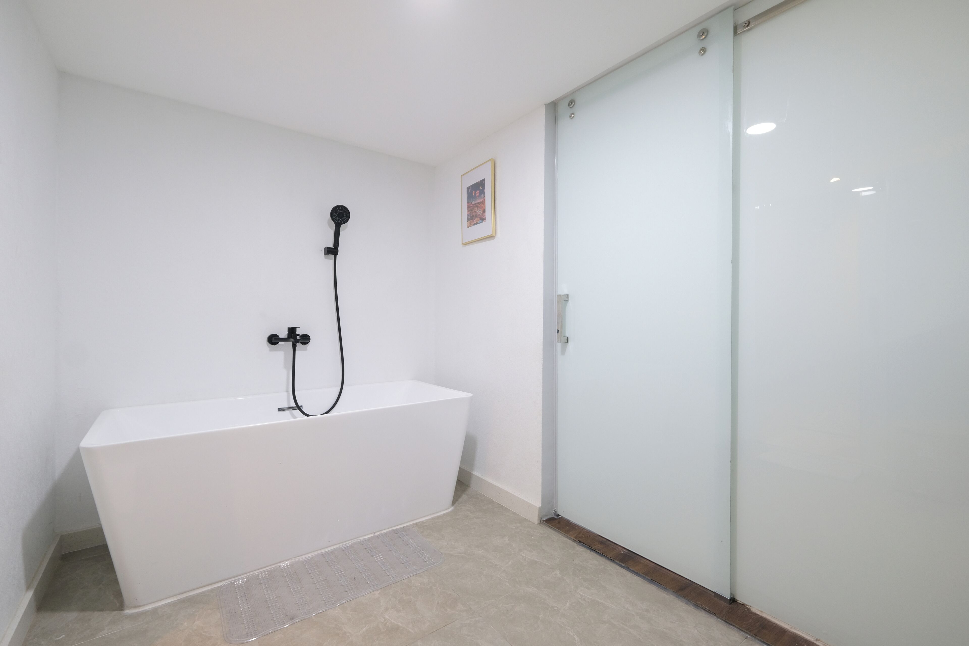 Un baño moderno con una bañera blanca, cabina de ducha con vidrio y una puerta con panel de vidrio esmerilado.