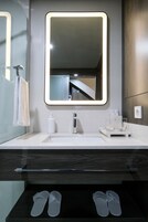Un baño moderno con un espejo grande, un lavamanos y un cajón con pantuflas.