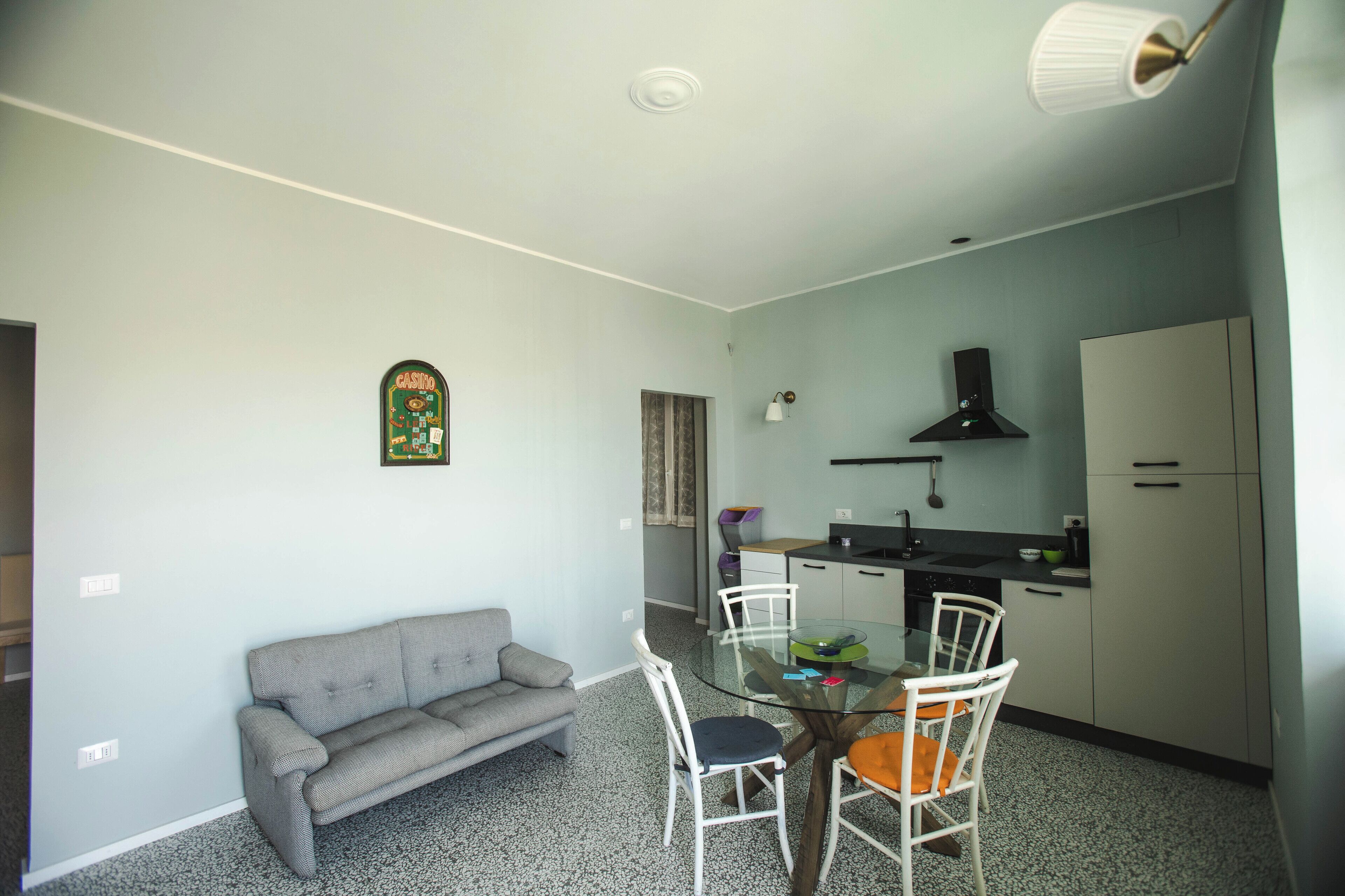 A compact living space with a kitchenette, a dining area with a glass table, a sofa, and a ceiling light fixture.