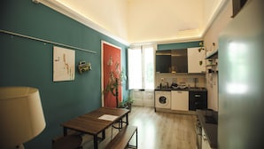 A compact kitchen with a washing machine, a dining area with a table and bench, and a red door. - 4Brooms-Paladini b&b (Lecce)