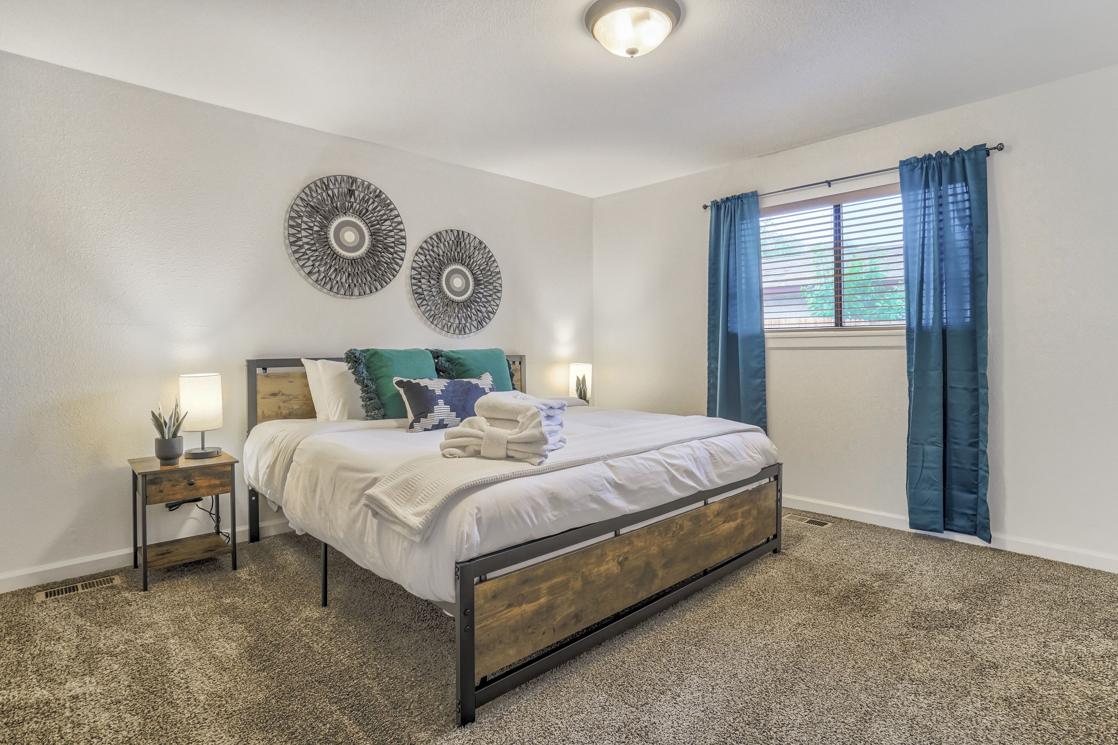 A bedroom with a bed, two wall decor pieces, a nightstand, a lamp, and a window with curtains.