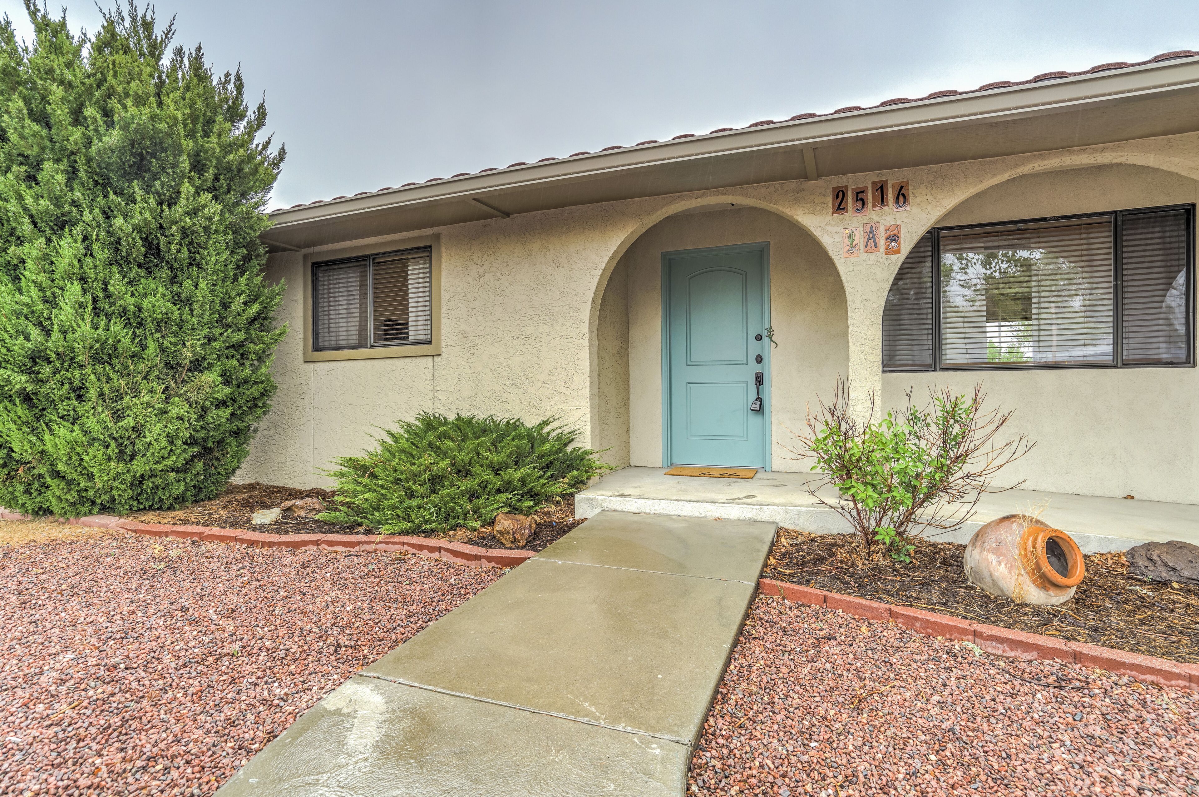 A single-story house with a blue door, a number '2516' above the door, and a small garden with gravel and plants.