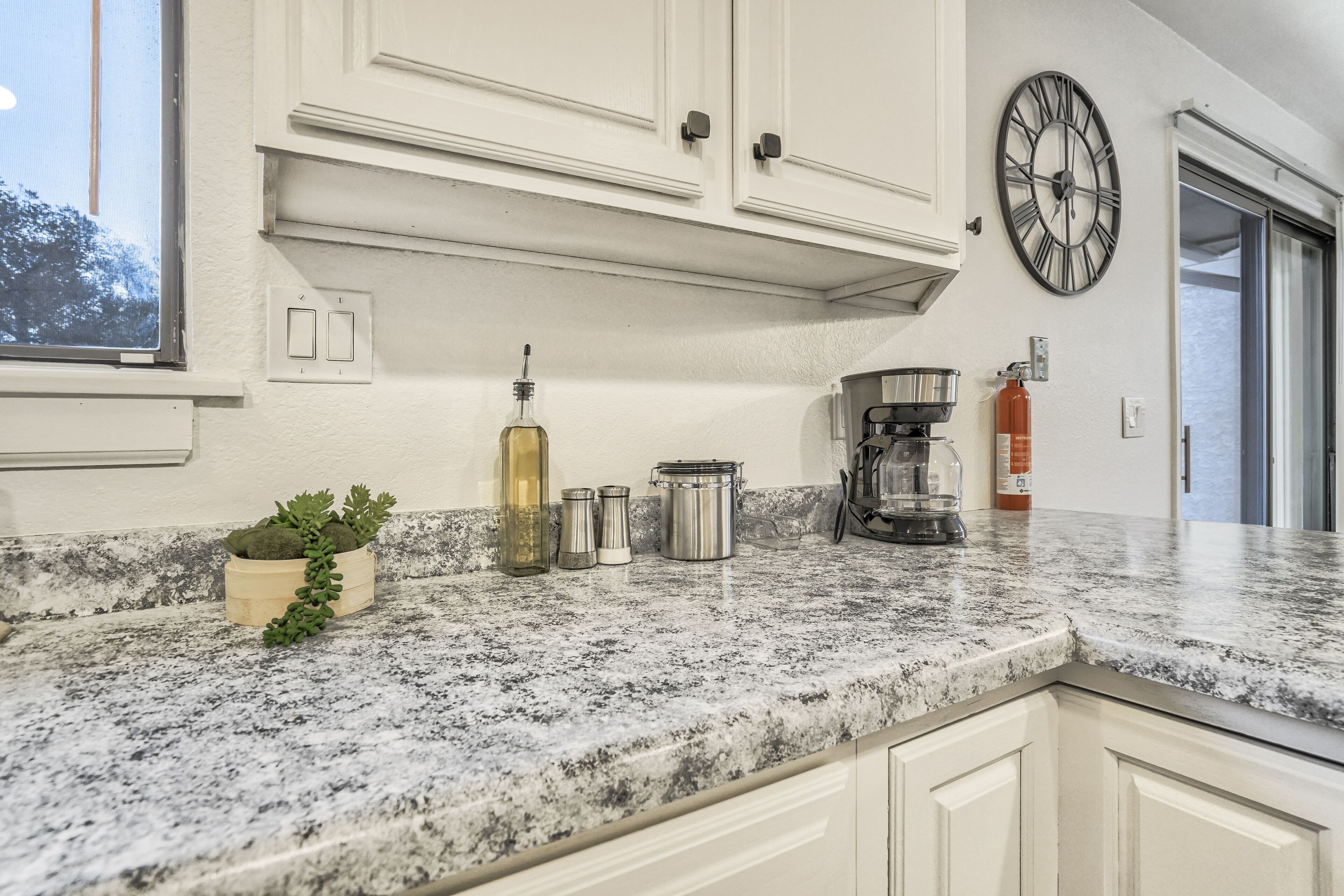 A kitchen with white cabinets, a granite countertop, a clock, and a window.