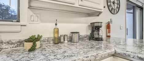 A kitchen with white cabinets, a granite countertop, a clock, and a window.