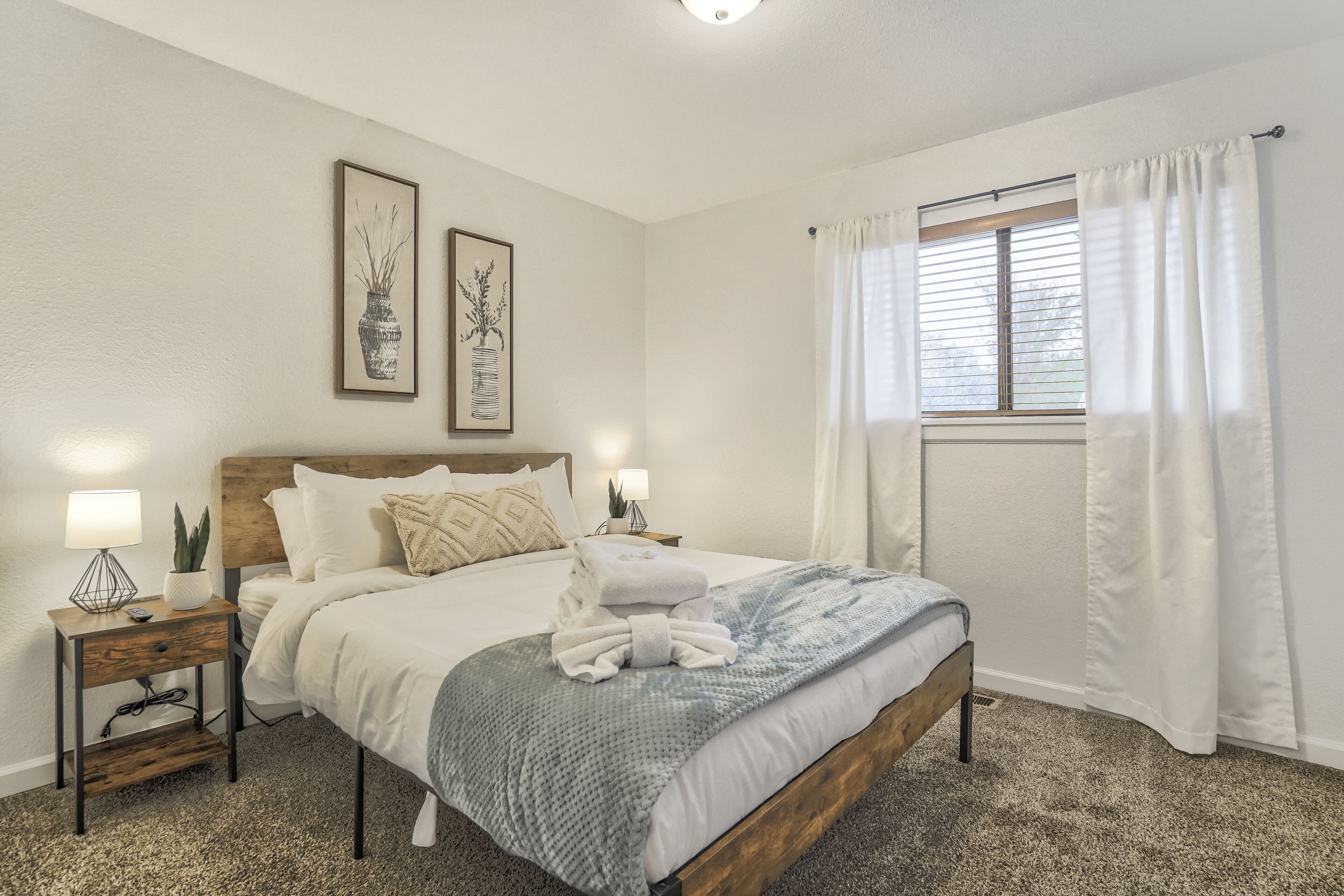 A neatly arranged bedroom with a bed, bedside tables, and artwork on the walls.