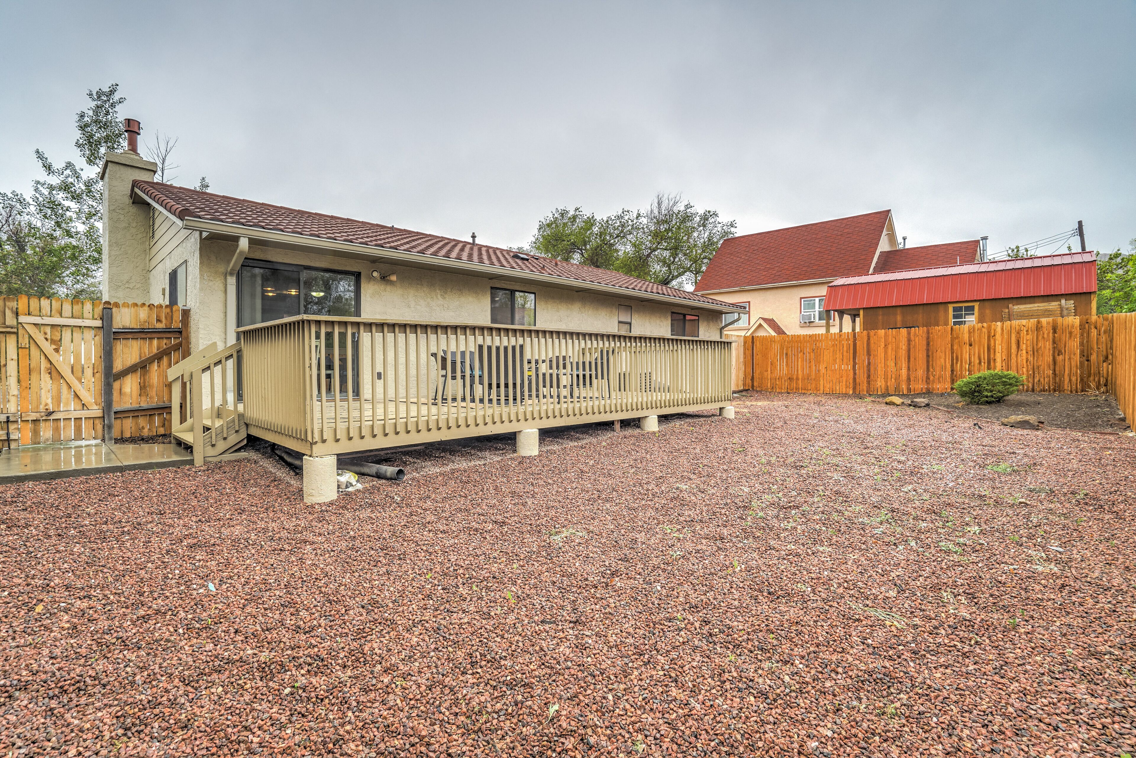 Une maison avec une terrasse en bois, une allée en gravier et un garage au toit rouge.