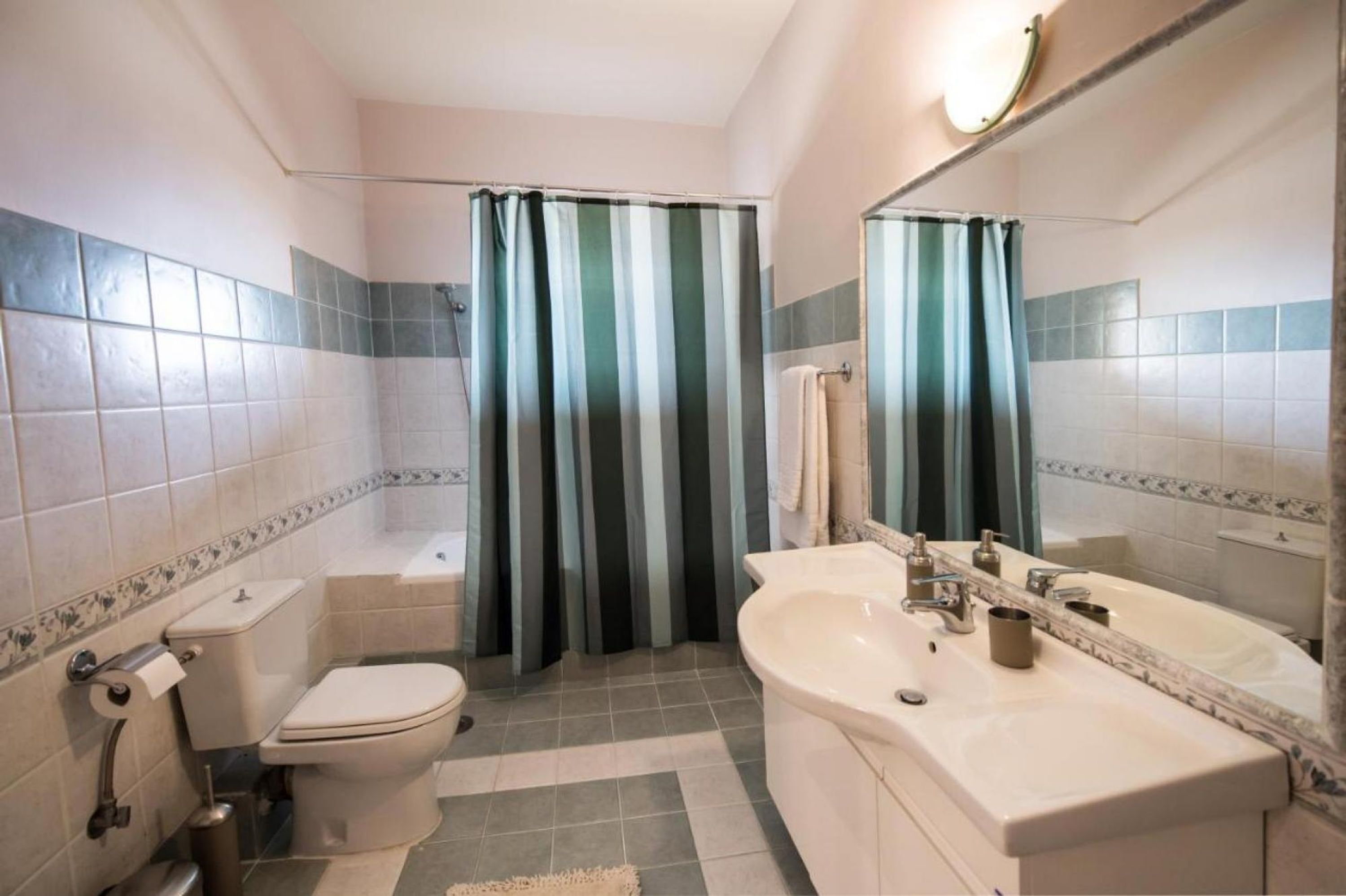 A bathroom with a toilet, sink, and bathtub, featuring striped curtains and tiled walls.
