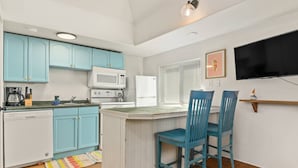 A compact kitchen with teal cabinets, a microwave, a refrigerator, and a small dining area with two blue chairs. - Outstanding Location, Pet Friendly, Kitchen, WiFi, Two Blocks From Beach, Unit 7 (Rockaway Beach)