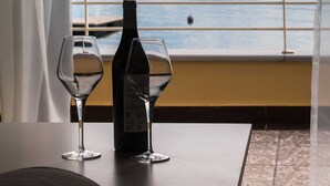 A table with two empty wine glasses and a bottle, set against a window with a view of mountains and water. - NV Seafront Studios AV Properties (Lefkada)