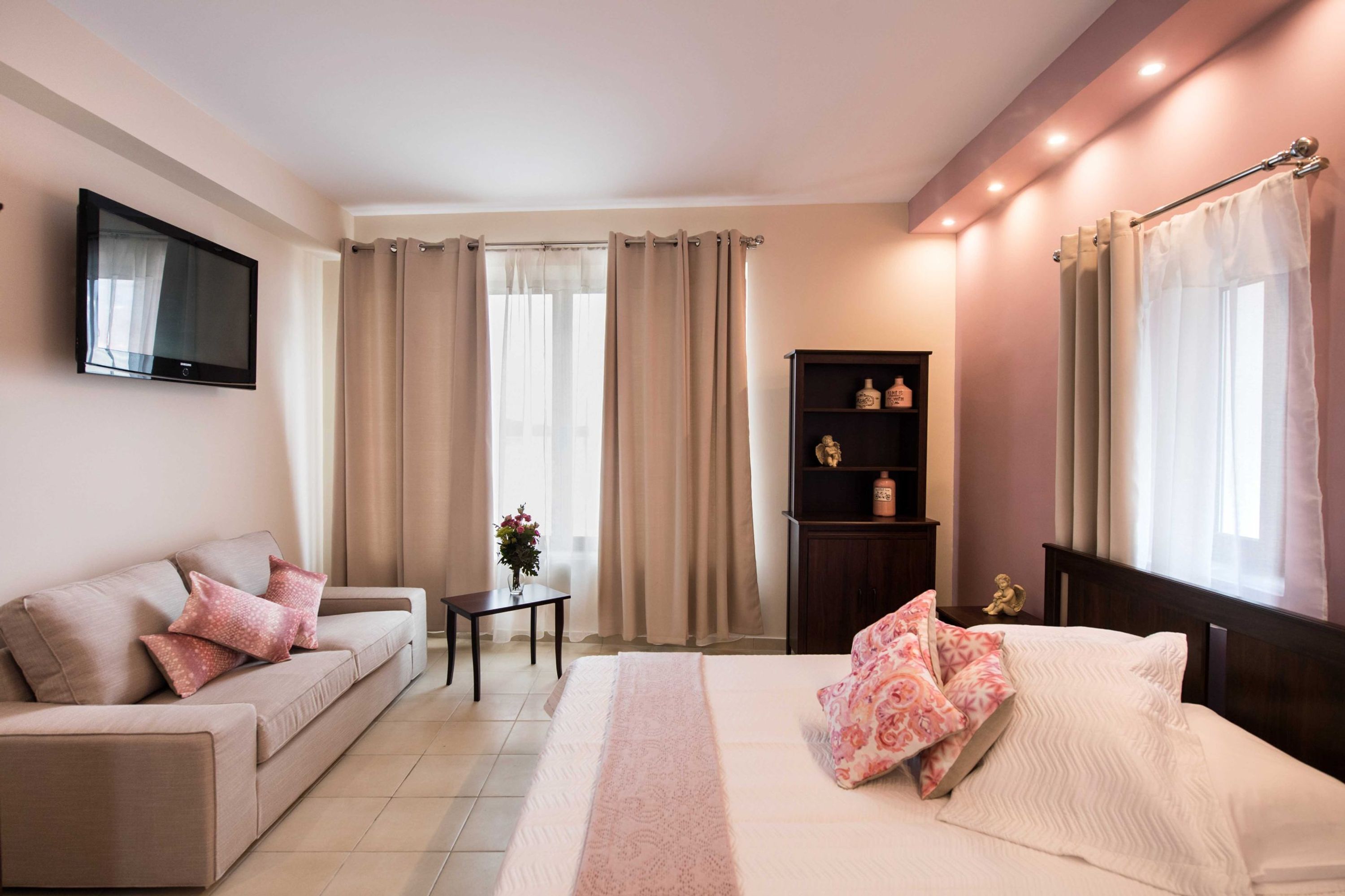 A modern hotel room with a bed, a sofa, a TV, and a small table with a vase.