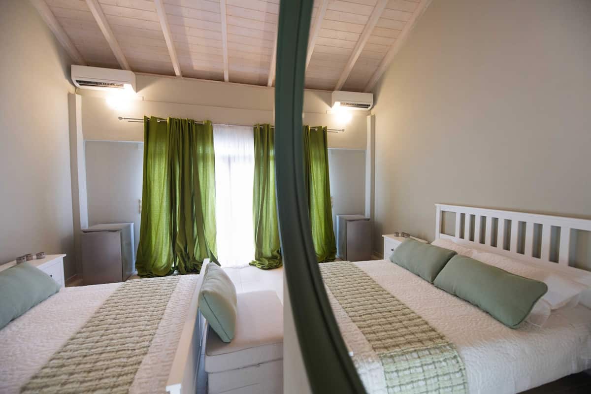 A bedroom with two beds, green curtains, white headboards, and bedside tables.