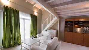 A modern living room with a white sofa, a dining table, and a staircase leading to a kitchen area. - NV Seafront Studios AV Properties (Lefkada)
