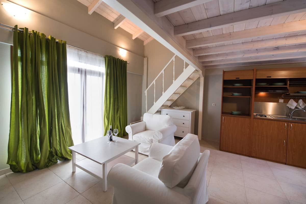 A modern living room with a white sofa, a dining table, and a staircase leading to a kitchen area.