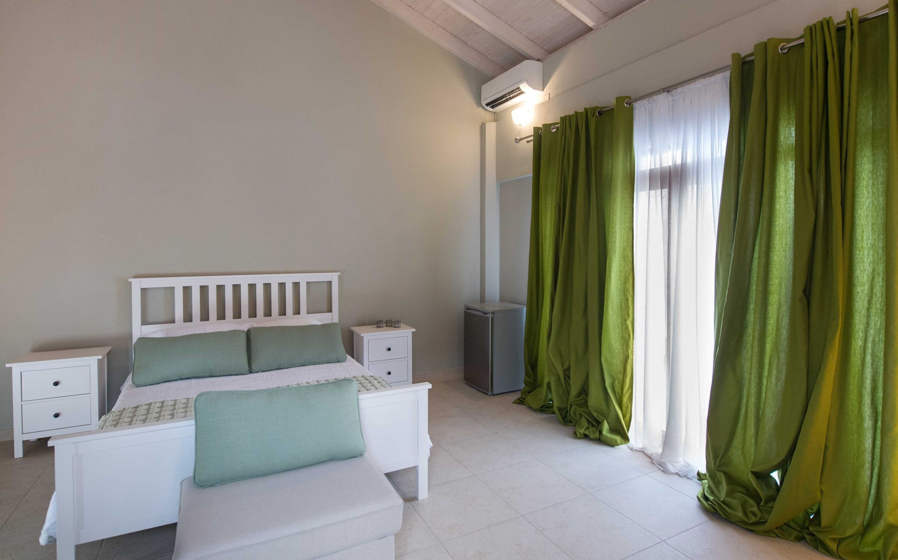 A bedroom with a bed, bedside tables, a mirror, and green curtains.