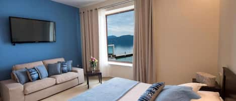 A hotel room with a bed, a sofa, a TV, and a window with a view of the sea.